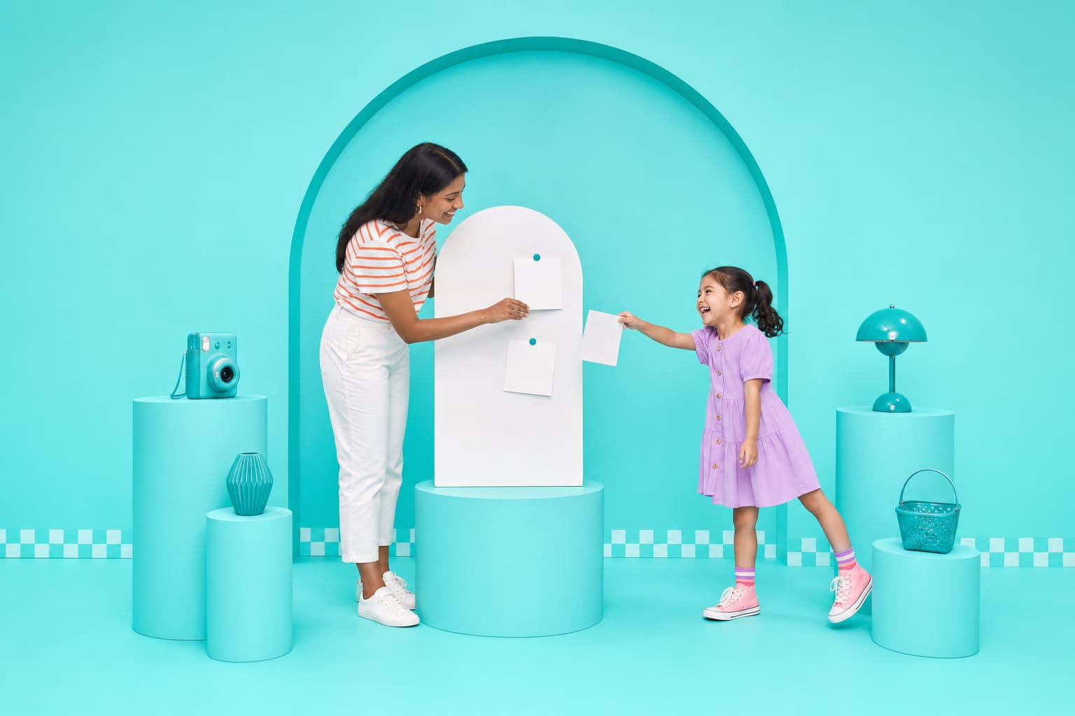 A studio owner pins photo cards onto a profile board while a laughing girl hands her one more in an aqua studio.